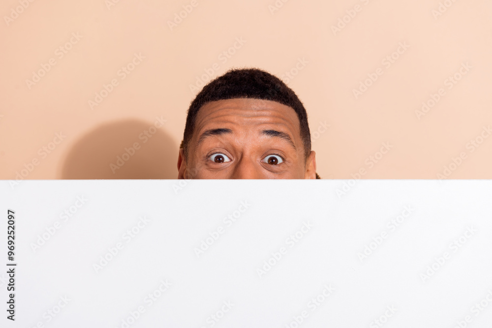Photo of crazy funny man wear trendy clothes hiding white wall empty space isolated on beige color background