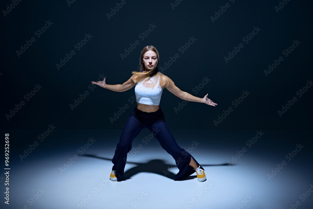 Obraz premium Youthful passion on display. Young energetic woman dancing hip hop with precision against navy blue studio background. Concept of freestyle dance, modernity, urban culture, youth