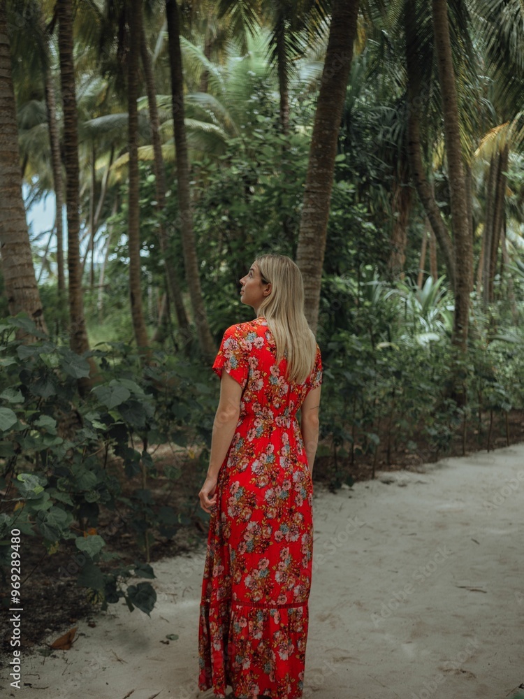 Woman in a red floral dress walking through a tropical forest with tall palm trees. Woman in a red floral dress walking through a tropical forest with tall palm trees.