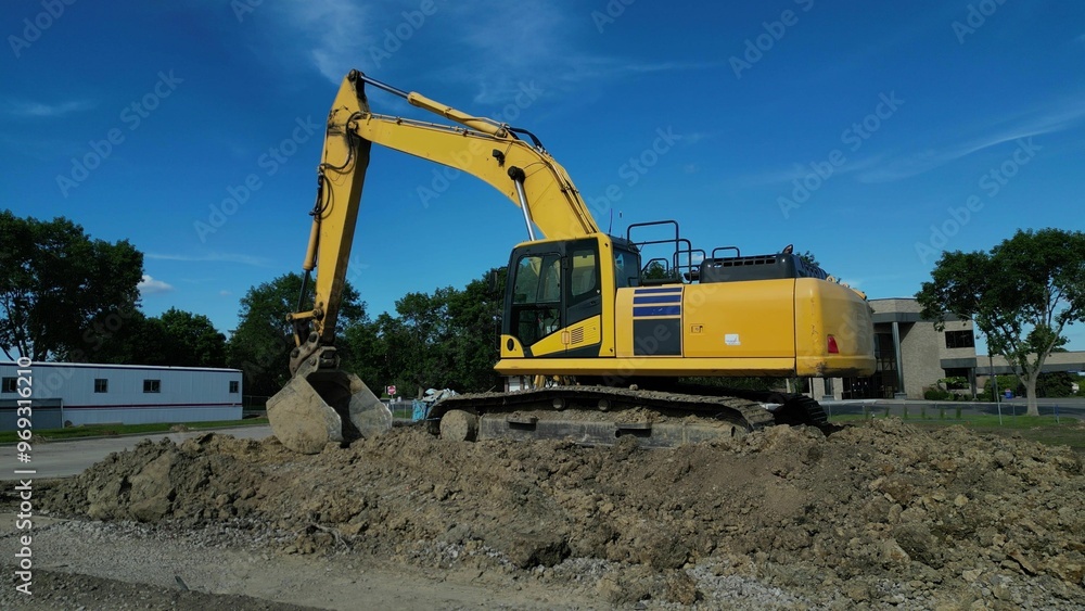 Obraz premium Yellow excavator on a dirt hill in a construction site, on a clear sunny day.