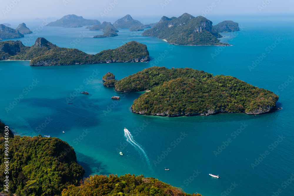 Fototapeta premium The beautiful landscape showcases turquoise waters surrounding dense green islands, with a small boat traversing the calm sea under a vibrant blue sky