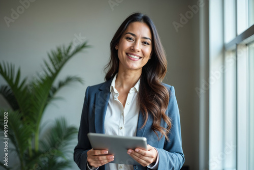 Portrait of young Hispanic professional business woman standing in office. Happy female company executive, smiling businesswoman entrepreneur corporate leader manager looking at camera using tablet