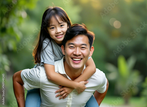 Happy asian family - father giving daughter piggyback ride in park
