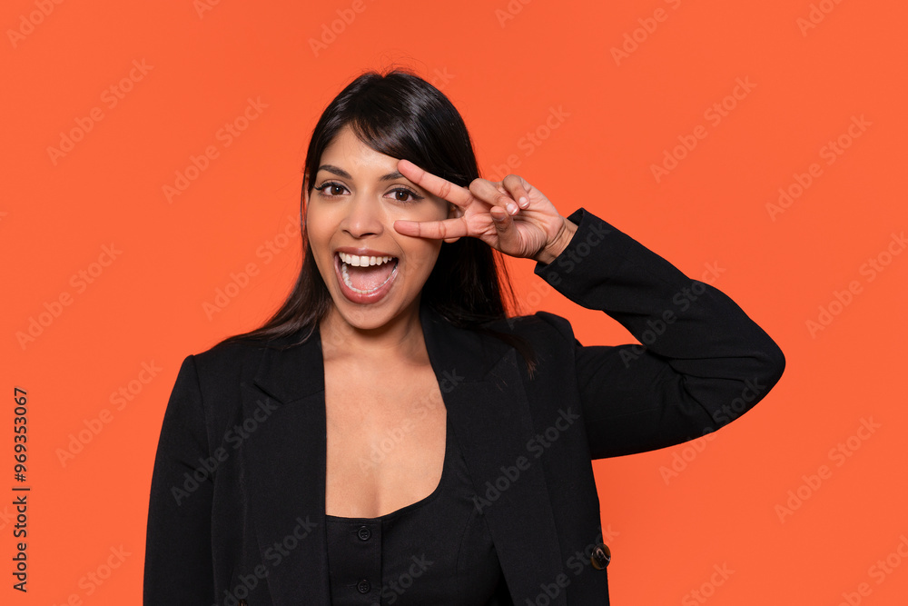 Joyful Woman Making Peace Sign Against Vibrant Orange Backdrop During Cheerful Moment Joyful Woman Making Peace Sign Against Vibrant Orange Backdrop During Cheerful Moment