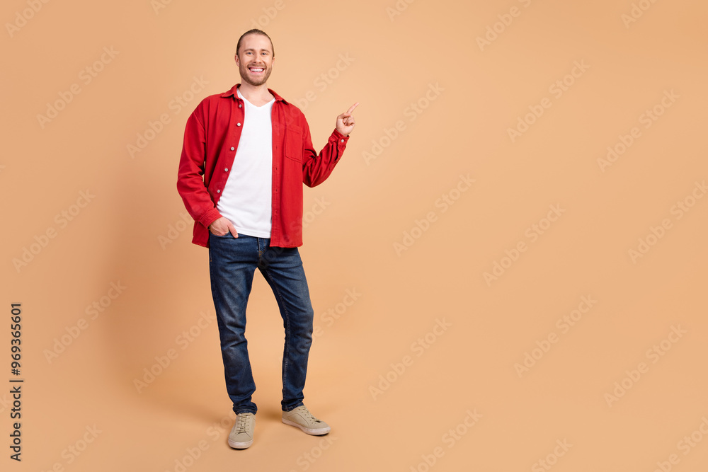 Full size photo of nice young man indicate finger empty space wear red shirt isolated on beige color background Full size photo of nice young man indicate finger empty space wear red shirt isolated on beige color background