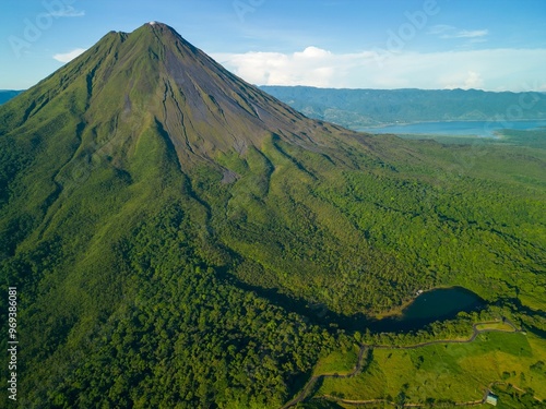 View of Arenal Volcano surrounded by lush green forest and a clear blue sky in Costa Rica photo