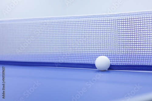 A white ping pong ball is placed on a ping pong table with a net behind it. A white ping pong ball with blurred background. photo