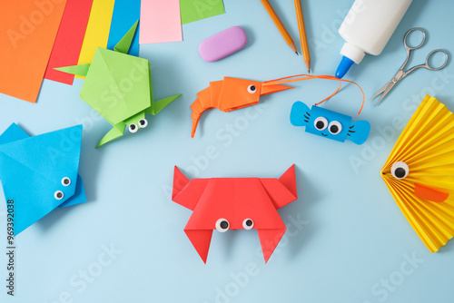 Finished origami red paper toy crab. On the table are other finished toys fish, stingray, turtle, shrimp. Around the stationery for paper art scissors, glue, colored sheets.