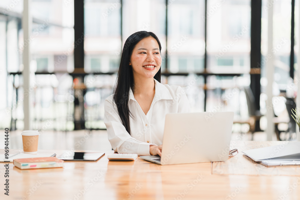 A professional woman smiles while working on laptop in modern office A professional woman smiles while working on laptop in modern office