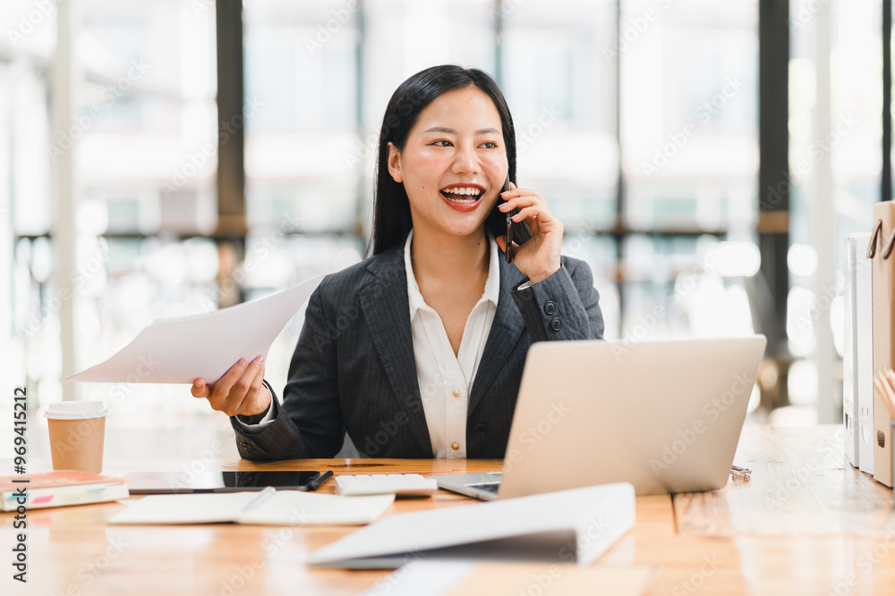 A professional woman is engaged in phone conversation while managing documents at her desk A professional woman is engaged in phone conversation while managing documents at her desk