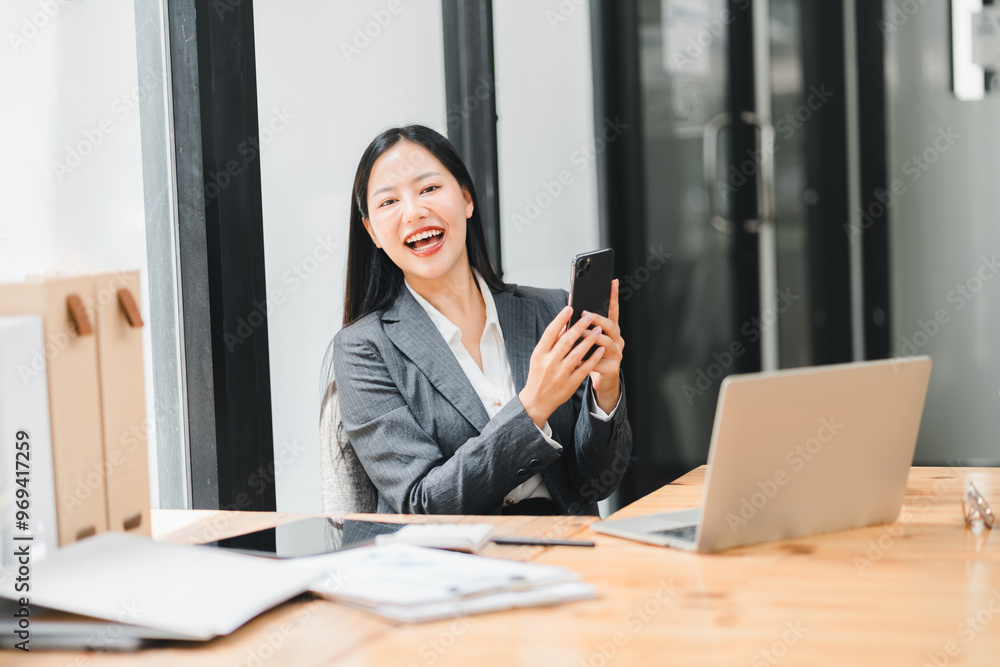 A joyful woman in suit smiles while using her smartphone at modern office desk A joyful woman in suit smiles while using her smartphone at modern office desk