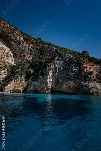 Vertical scenic view of a blue sea waters with rocky shoreline on a sunny day with blue sky