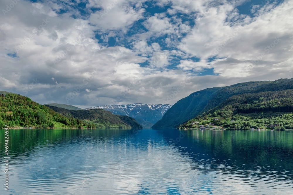 Scenic view of a fjord with mountains and a partly cloudy sky reflecting on the water in Norway Scenic view of a fjord with mountains and a partly cloudy sky reflecting on the water in Norway