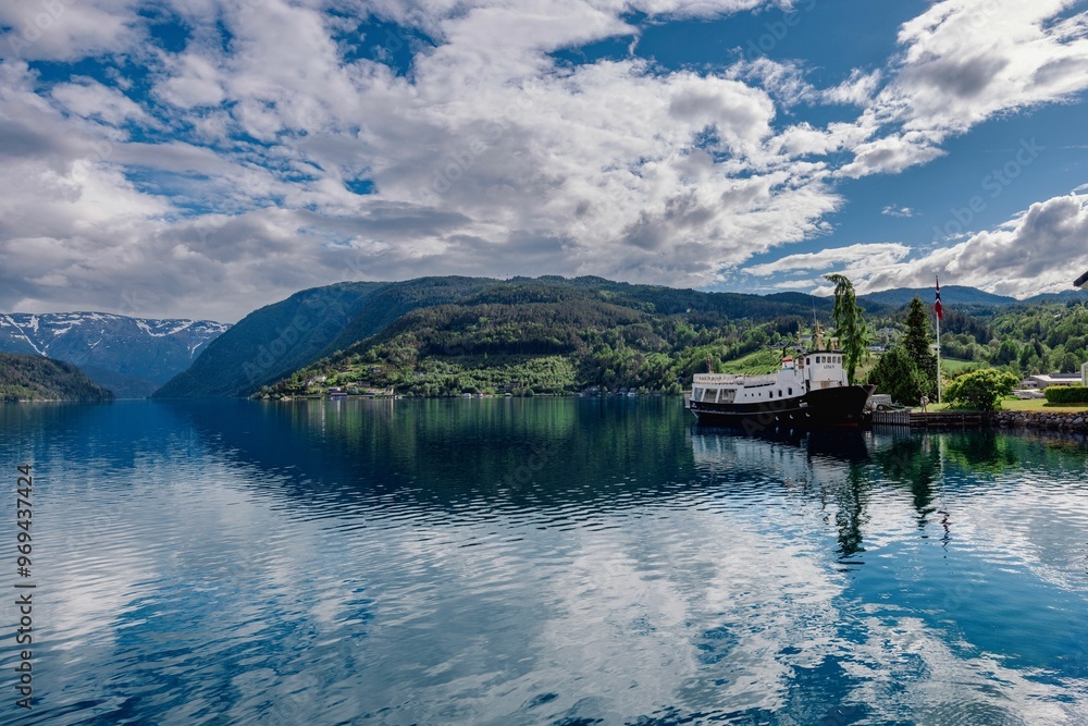 Scenic view of a fjord in Norway with a boat docked, surrounded by mountains Scenic view of a fjord in Norway with a boat docked, surrounded by mountains