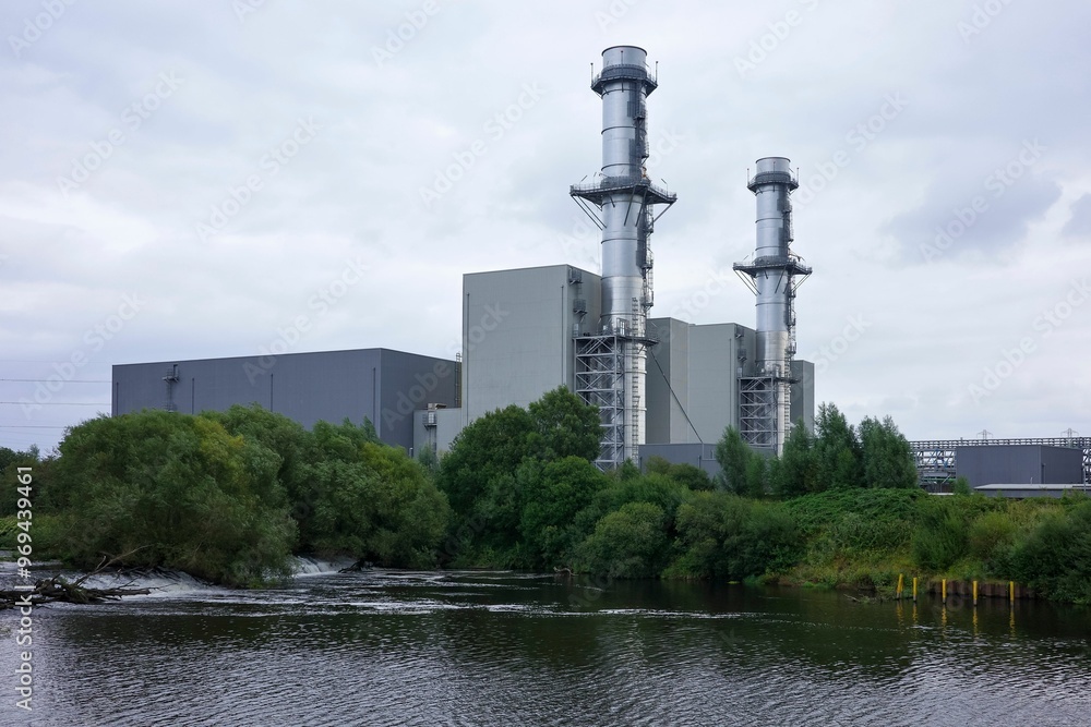 Industrial power plant with two tall chimneys near a river on a cloudy day. Industrial power plant with two tall chimneys near a river on a cloudy day.