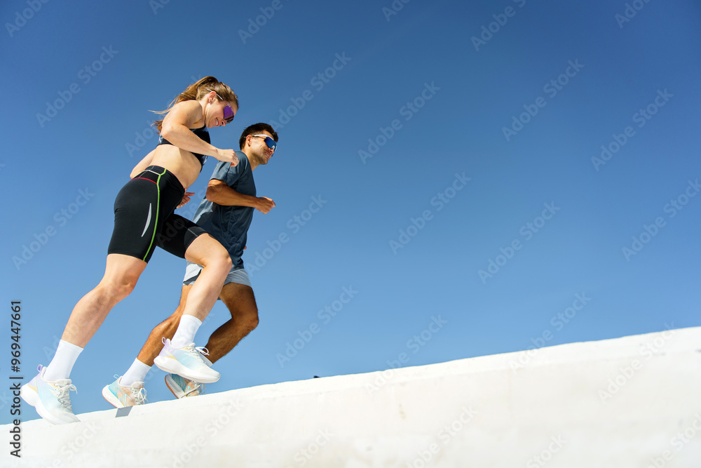 Two athletes descending white stairs outdoors, focused on maintaining their pace, with a bright blue sky above. Two athletes descending white stairs outdoors, focused on maintaining their pace, with a bright blue sky above.