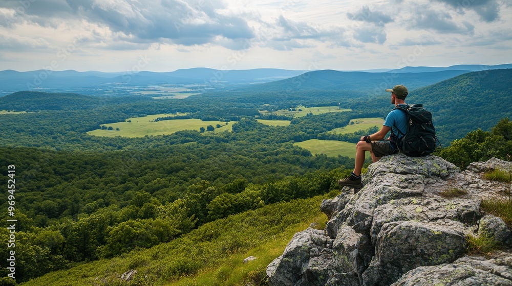 A hiker taking a break on a rock outcrop with a wide view of a green valley and distant mountains A hiker taking a break on a rock outcrop with a wide view of a green valley and distant mountains