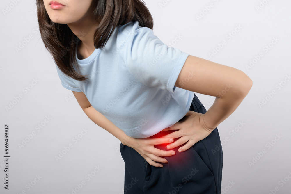 Experiencing abdominal pain, woman in blue shirt holds her side, indicating discomfort. This image captures emotional expression of distress and concern Experiencing abdominal pain, woman in blue shirt holds her side, indicating discomfort. This image captures emotional expression of distress and concern