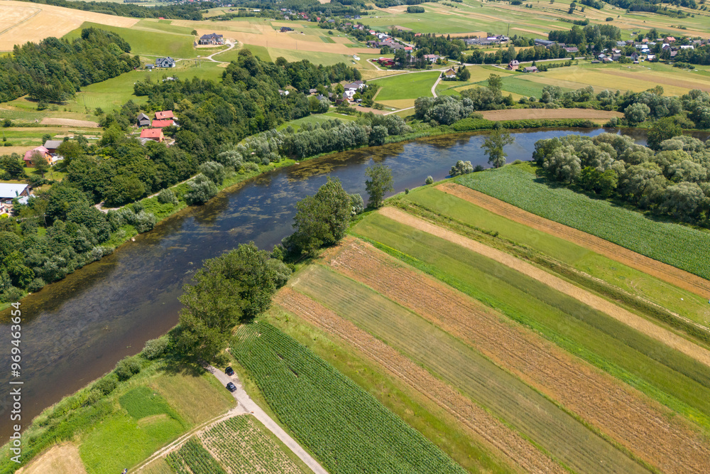 Drone aerial perspective of a river flowing through the Polish countryside in summer, surrounded by green foliage. Drone aerial perspective of a river flowing through the Polish countryside in summer, surrounded by green foliage.
