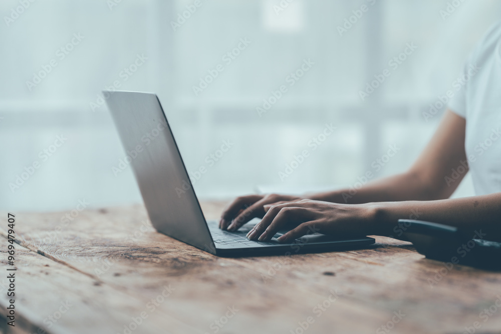 Fototapeta premium Focused Productivity: Hands typing on a laptop, bathed in natural light, on a rustic wooden desk, evoking a sense of quiet concentration and remote work efficiency. 