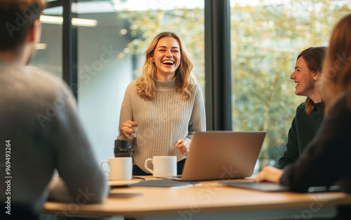 Wallpaper Mural A group of young professionals laugh together during a meeting in a modern office space. They are sitting around a table with laptops, coffee mugs, and a relaxed atmosphere. Torontodigital.ca