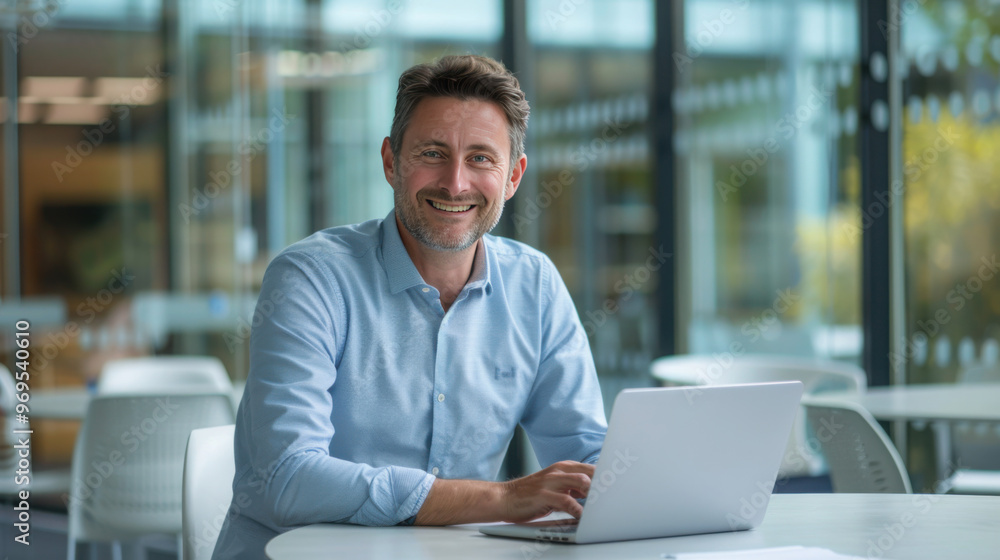 Centered view Portrait of A attractive professional man in his fourties, smiling and sitting at an office desk with open laptop on it. Centered view Portrait of A attractive professional man in his fourties, smiling and sitting at an office desk with open laptop on it.