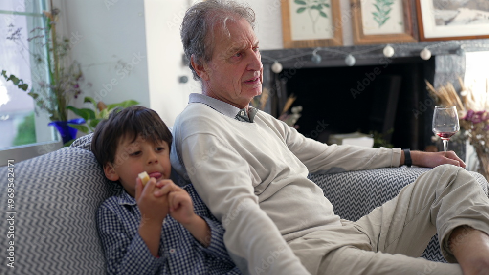 Grandfather and young boy enjoying quiet time on the couch, with the grandfather looking thoughtful and the boy focused on eating a snack, highlighting intergenerational connection Grandfather and young boy enjoying quiet time on the couch, with the grandfather looking thoughtful and the boy focused on eating a snack, highlighting intergenerational connection