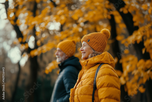 Elderly pair man and woman on the fall walk in the wood or park, orange earth tones and trees at the background, caps on the head. 