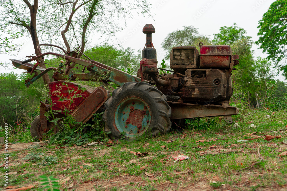 old, rusty motor cultivator overgrown with vegetation, abandoned in forested area with trees and shrubs in background.