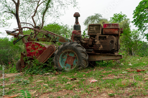 Obraz na płótnie old, rusty motor cultivator overgrown with vegetation, abandoned in forested area with trees and shrubs in background. w salonie