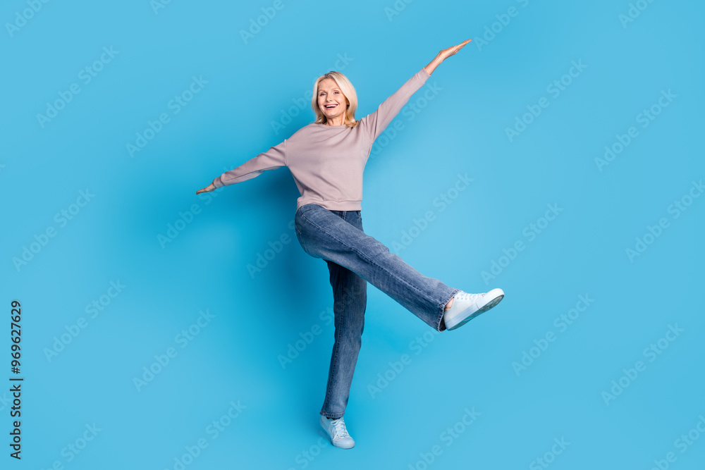 Full body photo of lovely senior lady spread hands flying dancing dressed stylish gray garment isolated on blue color background Full body photo of lovely senior lady spread hands flying dancing dressed stylish gray garment isolated on blue color background