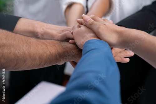 Group of diverse office worker join hand together in office room symbolize business synergy and strong productive teamwork in workplace. Cooperation and unity between business employee. Prudent