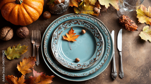 A beautiful fall table setting with plates, silverware, and autumn decorations like leaves, a pumpkin, and acorns on a brown background. photo