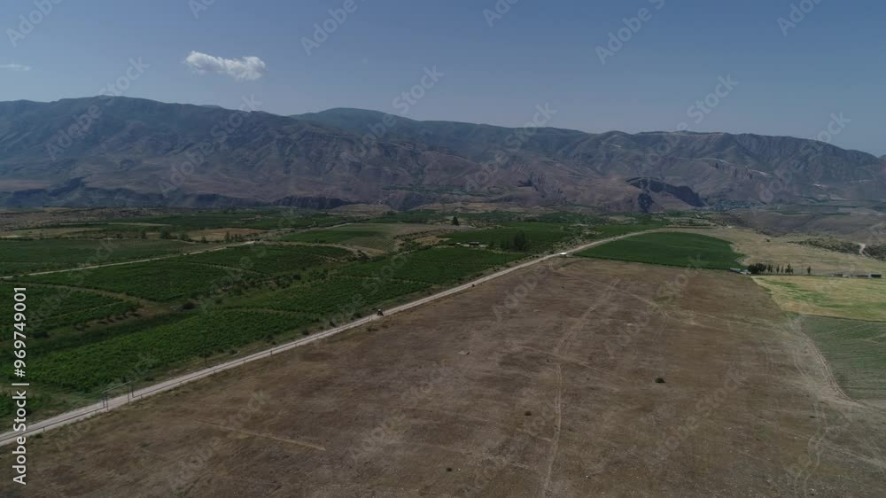 Drone pullout of a vast rural field with a road, and mountain with blue sky in the background Drone pullout of a vast rural field with a road, and mountain with blue sky in the background