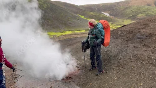 A group of hikers trekking through Iceland's steaming geothermal landscapes, showcasing volcanic terrain and vibrant moss-covered hills. photo