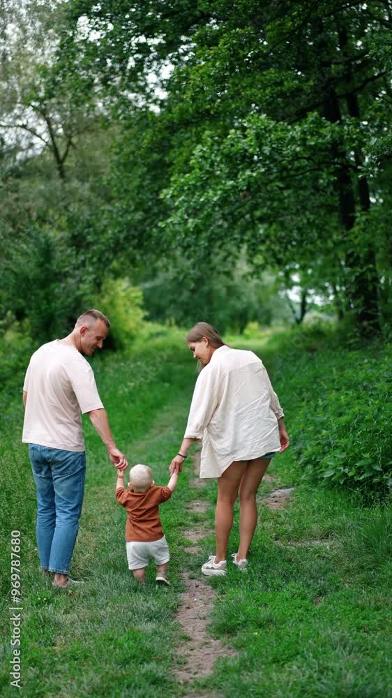 Mother and father leading their baby boy learning to walk. Family of three in the nature in summer. Vertical video. Mother and father leading their baby boy learning to walk. Family of three in the nature in summer. Vertical video.