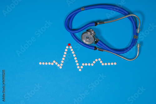 Medical ECG heart wave made from white tablets against a blue background. A stethoscope adds to the clinical concept. Editorial medical heart related picture. EKG cardiac trace. photo