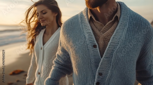 Cinematic shot of an attractive man wearing a light blue cardigan sweater walking with his wife on the beach