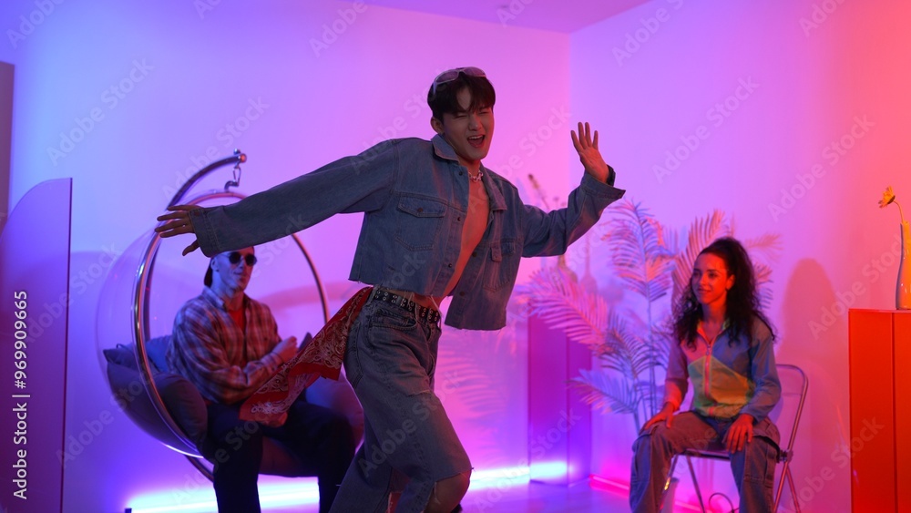 Fototapeta premium Skilled asian dancer moving to modern music while multicultural friend sitting at chair. Professional performer dancing show energetic foot step while hipster team cheering and supporting. Regalement.