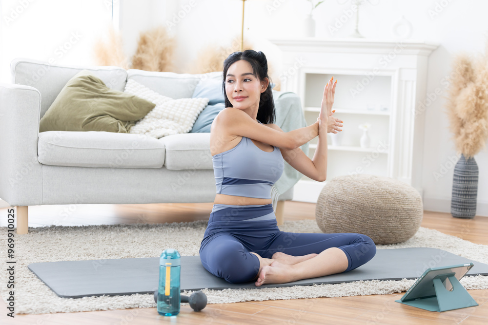 Asian woman sitting on yoga mat doing shoulder stretching exercise at home Asian woman sitting on yoga mat doing shoulder stretching exercise at home