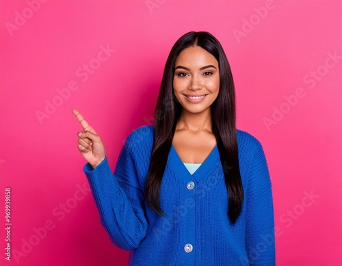 portrait of a woman smiling, wearing a blue dress pointing something on the empty magenta wall behind her 