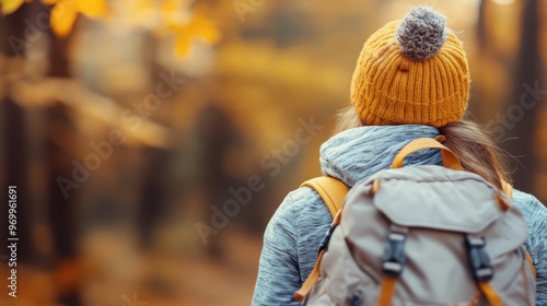 A person with a backpack is seen from behind, facing a forest wrapped in autumn's warm hues, highlighting the solitude and introspection associated with nature walks in fall.