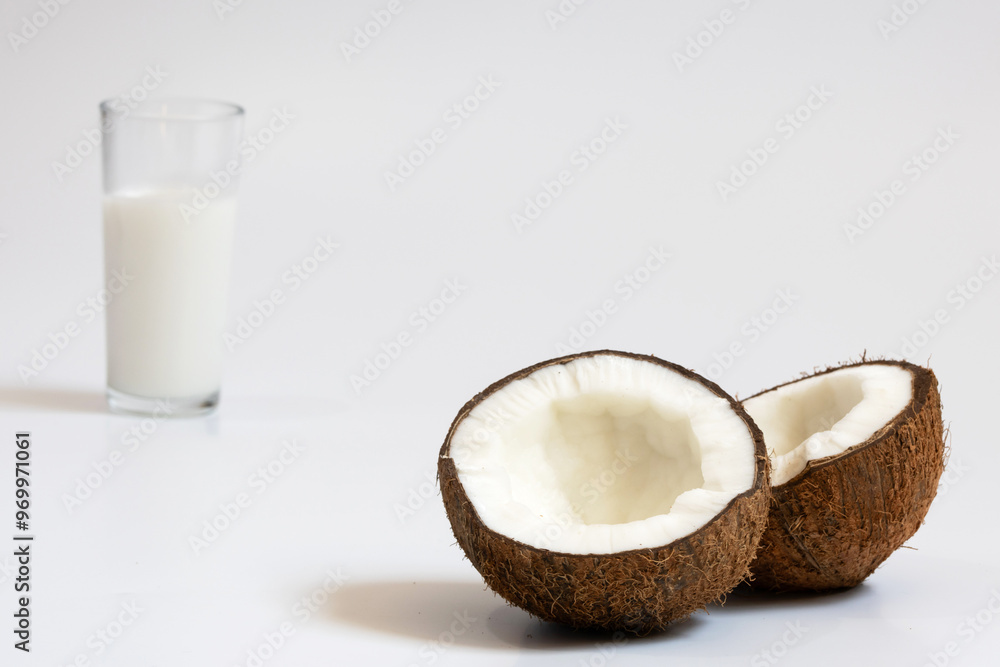 Two parts of a ripe coconut with very thick pulp in the foreground, and a glass with coconut milk in the background and out of focus Two parts of a ripe coconut with very thick pulp in the foreground, and a glass with coconut milk in the background and out of focus