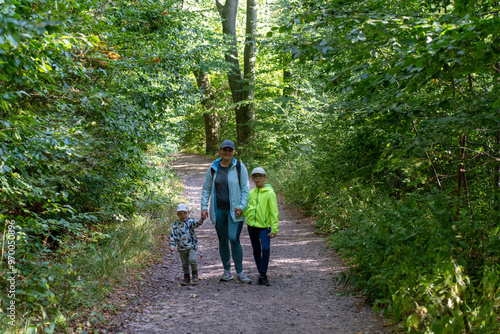 Mother with two children walking on a forest path during a sunny day, enjoying nature and spending time together outdoors. Concept of family bonding, outdoor activities, and healthy lifestyle. High