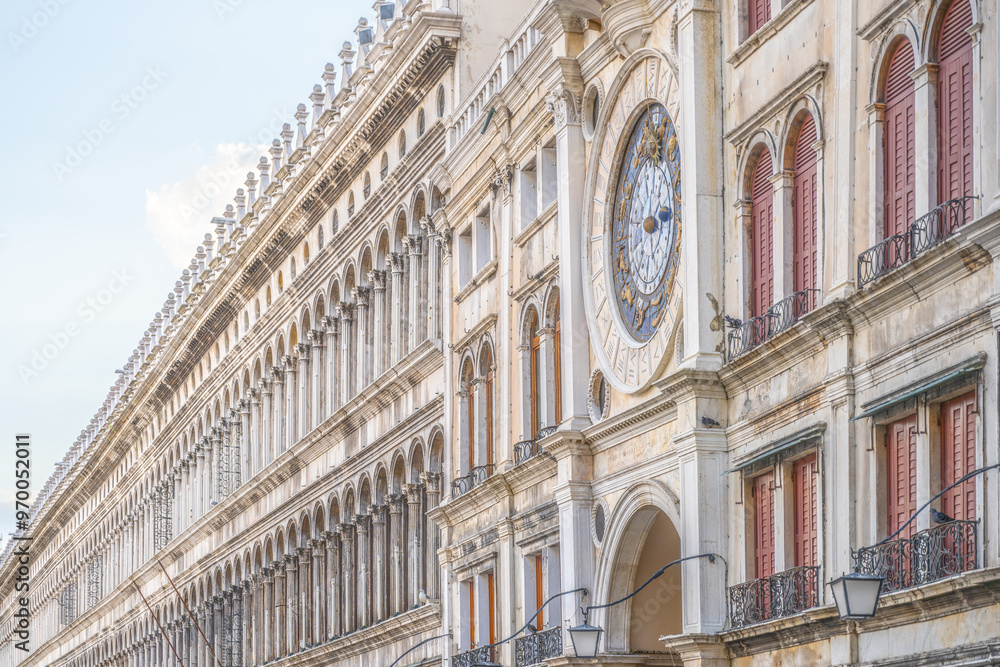 Fototapeta The early Renaissance St Marks Clocktower graces the Piazza San Marco's entrance with its intricate design and colorful clock. Tourists stroll by, enjoying the historic architecture of Venice.