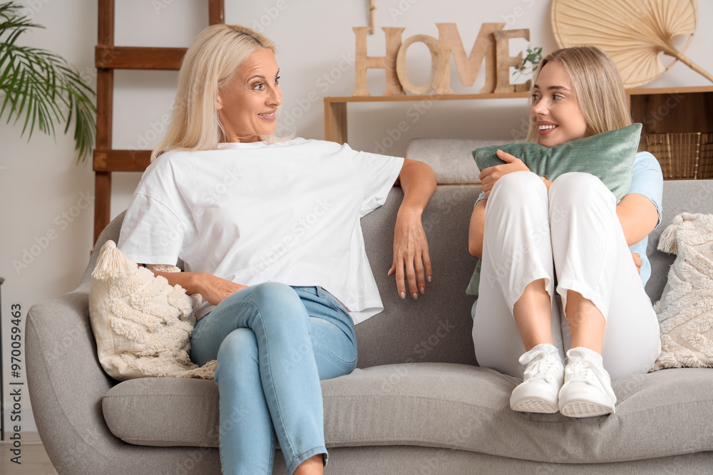 Young beautiful woman with her mother sitting on sofa in living room and spending time together Young beautiful woman with her mother sitting on sofa in living room and spending time together