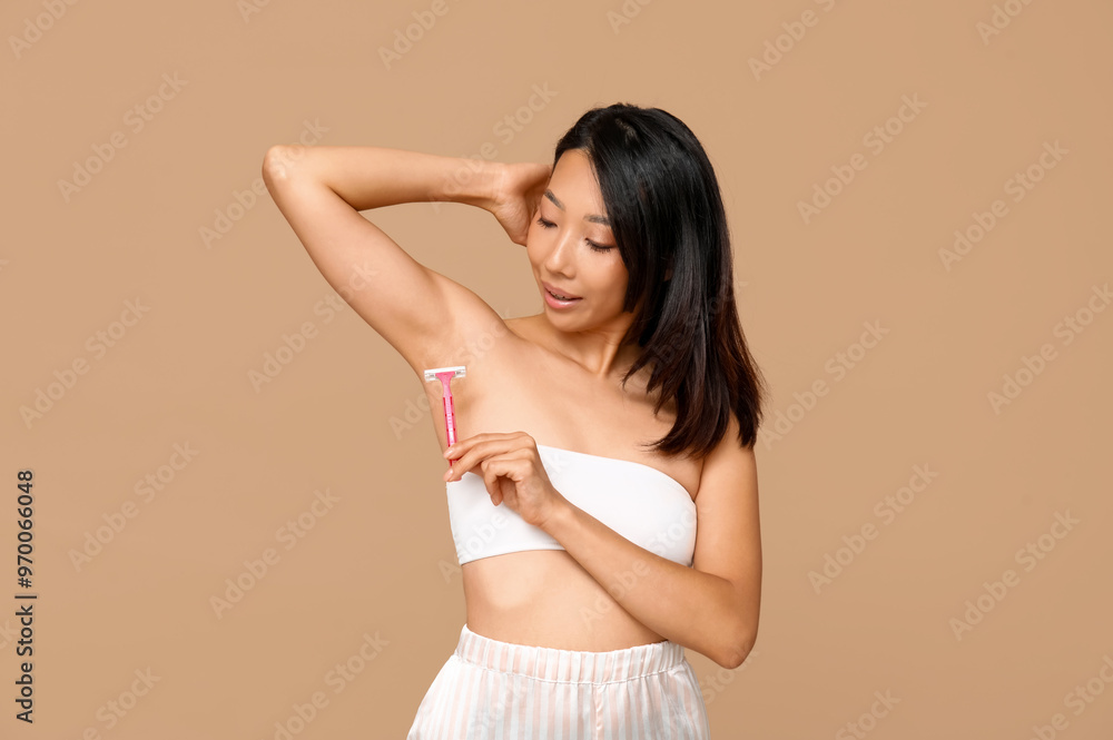 Young Asian woman with razor shaving underarms on brown background Young Asian woman with razor shaving underarms on brown background