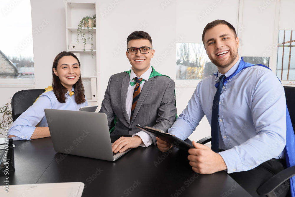 Business people with superhero capes working at table in office Business people with superhero capes working at table in office