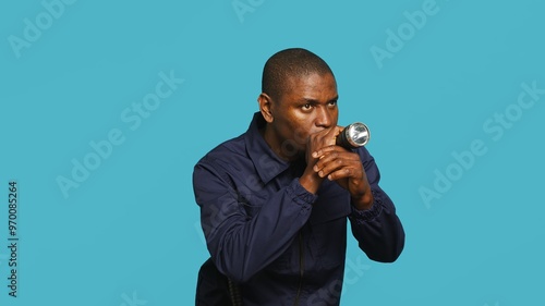 Portrait of security guard overseeing premises to prevent intrusion turning on flashlight to detect suspects. Private law enforcement worker using lantern device, studio backdrop, camera A