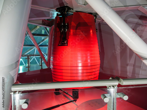 Red tuned mass damper pendulum is installed on the top floor of a high-rise structure, designed to reduce the building's oscillations during high winds or seismic activity and ensure stability.